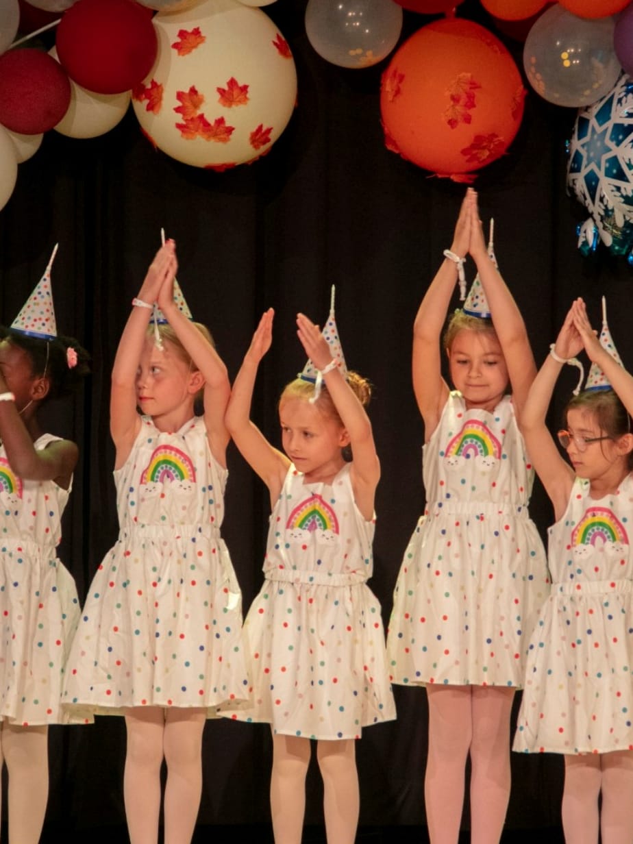 Kinderballett: Mädchen in weißen Kleidern mit erhobenen Armen bei einem Auftritt
